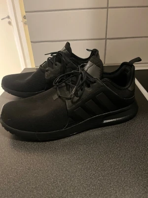 Svarta sneakers med mesh och syntet - Säljer ett par helsvarta sneakers med klassisk låg profil och snörning. Skorna har ovandel i mesh och syntetmaterial, samt diskreta detaljer på sidan. Perfekta för dig som gillar en clean och sportig look.