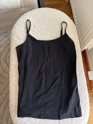 Svart linnetopp från Basic You - En svart, enkel linnetopp från Basic You i ekologisk bomull. Toppen har smala axelband och rak passform, perfekt att styla med jeans eller kjol. Mjuk och bekväm känsla tack vare materialet.