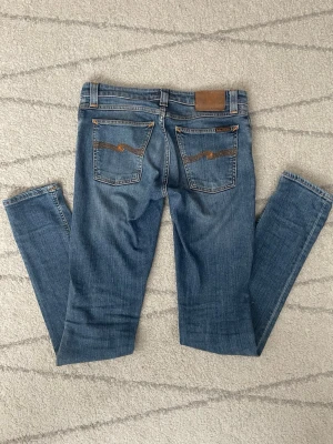 Blås nuddie jeans - Säljer ett par klassiska blå jeans med raka ben och snygga kontrastsömmar på bakfickorna. Jeansen har normal midja och är gjorda i ett mjukt denimtyg. Perfekta till en avslappnad stil och passar till det mesta.