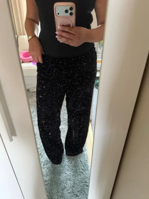 Svarta paljettbyxor med loose fit - Säljer ett par svarta byxor täckta med glittriga paljetter. Byxorna har en loose passform och rak siluett, perfekta för dig som vill sticka ut. Materialet är syntet och de har en riktigt snygg partyvibe. Bodens säljs också i en annan annons