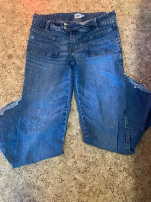 Blåa vida jeans med råa kanter - Säljer ett par blåa jeans med bred passform och råa, fransiga benslut. Jeansen har stora framfickor och ganska mid waist. Perfekta för en avslappnad och trendig look. Materialet är klassisk denim i bomull. avklippta då dom var för långa🤗