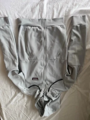Ljusgrå hoodie med dragkedja - Snygg ljusgrå hoodie från McKenzie med dragkedja framtill och två fickor med dragkedja. Tröjan har huva med svarta dragsnören och ribbade muddar vid ärmslut och nederkant. Perfekt för en avslappnad och stilren look.