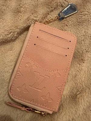 Rosa plånbok med dragkedja - Snygg rosa plånbok i läderimitation och dragkedja. Plånboken har ett fack på utsidan och en metallhake för att fästa i nyckelknippa eller väska. Perfekt storlek för kort och mynt.