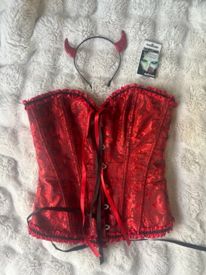 Djävuls outfit set med korsett, 1 röd lins och horn - Säljer min halloween outfit som en djävul. Oanvänd lins och oanvänd horn. Köpte det för 250 ish. Finns ej att köpa längre. Säljer var för sig på min profil