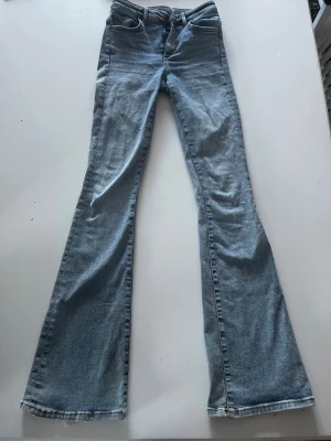 Ljusblå utsvängda jeans XS - Säljer ett par ljusblå jeans med utsvängda ben och hög midja. Jeansen har klassisk femficksdesign och är tillverkade i denim med en snygg tvätt. Perfekta för dig som gillar retrostil och vill ha ett par bekväma och trendiga jeans.
