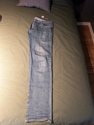 Levis 501 - Säljer ett par ljusblå jeans med rak passform och klassisk femficksdesign. Jeansen har normal midja och är tillverkade i denim med lätt tvättad look. Perfekta för en avslappnad och stilren outfit.