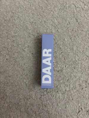 DAAR Cosmetics Purple Vanilla läppbalsam - Snyggt läppbalsam från DAAR Cosmetics i färgen Purple Vanilla. Förpackningen är stilren i lila med vit text. Perfekt för dig som vill ha en unik och trendig färg på läpparna. Läppbalsam kommer i klassisk hylsa.