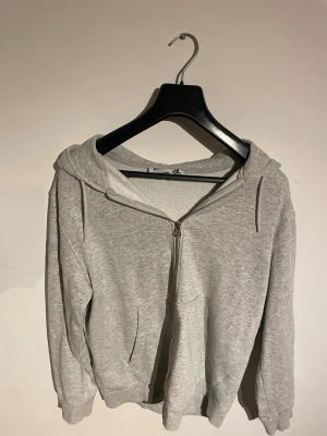 Ljusgrå zip hoodie med huva - En basic ljusgrå hoodie från Weekday med dragkedja framtill och två fickor. Hoodien har en klassisk huva med dragsko och ribbade muddar vid ärmar och nederkant. Perfekt för en avslappnad och chill stil. Nypris 800kr
