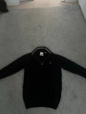 Gant half zip tröja - Svart långärmad tröja från gant med halv dragkedja och vit randdetalj på kragen. Tröjan har en liten broderad logga på bröstet och ribbade muddar vid ärmslut och nederkant. Perfekt för en stilren och avslappnad look. Knappast använd väldigt bra skick! Säljer för 300 kan med på priser ner till 200