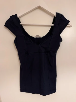 Mörkblå topp med djup urringning - Snygg mörkblå topp med korta ärmar och djup v-ringad urringning. Figurnära passform och stilren design, perfekt att matcha med jeans eller kjol. Materialet känns mjukt och stretchigt för en bekväm känsla.