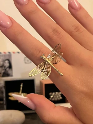 Guld trollslända ring 💍  - Unik ring i guldfärgad metall formad som en trollslända med detaljerade vingar och små stenar som ögon. Ringen har en iögonfallande design och passar perfekt för dig som gillar statement-smycken och naturinspirerade accessoarer.