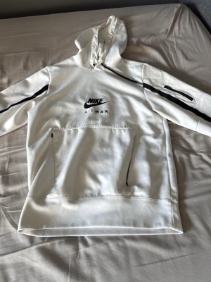 Vit Nike Air Max hoodie med svarta detaljer - Säljer en fräsch vit Nike Air Max hoodie med svarta detaljer och logga på bröstet. Hoodien har huva med dragsko, en stor magficka med dragkedjor och svarta ränder längs ärmarna. Perfekt för dig som gillar sportig och clean stil.