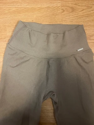 Ribbade beige leggings Aim'n - Supersnygga ribbade leggings i beige från Aim'n. Hög midja och stretchigt material som sitter skönt och formar sig efter kroppen. Perfekta för en trendig och avslappnad look. Metallogo framtill vid midjan.