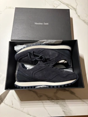 Mörkblå sneakers från Massimo Dutti ( helt nya )  - Stilrena mörkblå sneakers från Massimo Dutti i mocka med vita och blå detaljer på sulan. Klassisk låg modell med snörning och diskret design som passar till det mesta. Perfekta för dig som gillar en clean och modern look. Helt nya och är inte använda, köpta för 1500kr och säljer för 700 storlek 42