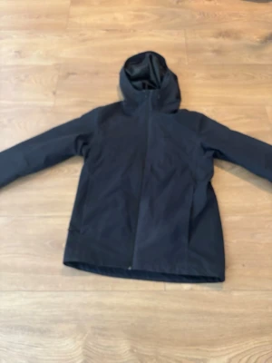 Svart vindjacka med huva - Snygg svart vindjacka med hel dragkedja och huva. Jackan har en minimalistisk design utan synliga loggor och är tillverkad i ett slätt, vindtätt material. Perfekt för blåsiga dagar och enkel att matcha med olika outfits.