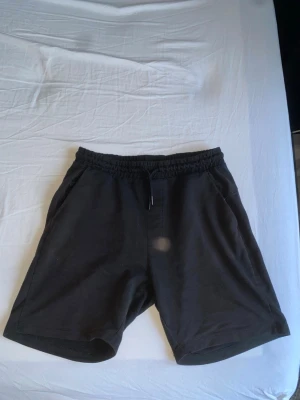 Svarta shorts med snörning - Svarta shorts med elastisk midja och snörning framtill. Klassisk passform med två sidofickor och raka ben. Perfekta för sommaren och tillverkade i mjukt bomullsmaterial för maximal komfort.