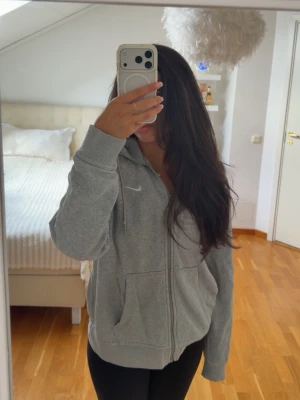 Grå zip hoodie från Nike - Säljer en grå zip hoodie från Nike med huva och dragsko. Hoodien har fickor framtill och en liten vit Nike-logga på bröstet. Perfekt för chill dagar eller när du vill ha en sportig look