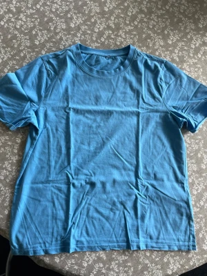 Blå basic t-shirt i bomull - En enkel blå t-shirt i mjuk bomull med rund hals och korta ärmar. Perfekt till jeans eller shorts för en avslappnad look. Klassisk passform och utan tryck eller mönster.