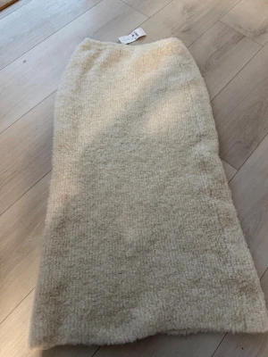 Beige halv lång kjol - (OANVÄND,PRISLAPP KVAR) EMysig beige långkjol i fluffigt fleecematerial. Kjolen har en rak och enkel design som ger en avslappnad och trendig look. Perfekt för dig som gillar bekväma och stilrena plagg med en twist.