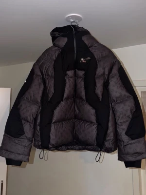 Svart och mörkbrun pufferjacka med mönster - Säljer en oversized pufferjacka i svart och mörkbrunt med diskret mönster över hela tyget. Jackan är i storlek M men passar även S. Oanvänd jacka,Perfekt för kalla vinterdagar.