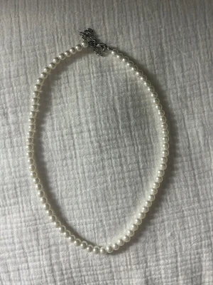 Pärlhalsband  - Säljer ett stilrent halsband med vita, runda pärlor och ett justerbart silverfärgat lås. Perfekt för dig som vill ha en tidlös accessoar som lyfter vilken outfit som helst. Pärlorna är jämnt placerade och ger ett elegant intryck.