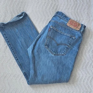 Levi's blå raka jeans - Klassiska blå Levi's jeans med rak passform och fem fickor. Jeansen har den ikoniska läderlappen bak i midjan och röd Levi's-tag på bakfickan. Tillverkade i slitstark denim, perfekta för en avslappnad och tidlös stil.