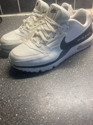 Nike Air Max vita sneakers - Snygga vita Nike Air Max sneakers med svart swoosh och AIR MAX-text på sidan. Skorna har en chunky sula med synlig luftbubbla och är gjorda i en mix av mesh och syntetmaterial.  Nästan helt oanvänd då dom inte passar mig längre. Nypris 1500