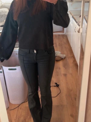 Svarta bootcut jeans med söm - Säljer ett par svarta bootcut skinnbyxor med markerad söm längs benen. Skinnbyxan har normal midja, klassiska fickor fram och bak samt knapp- och dragkedjestängning. 