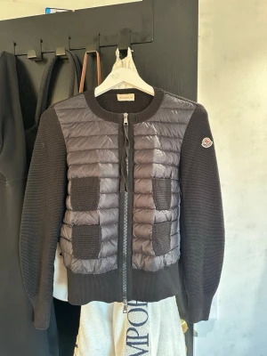 Svart cardiganjacka från Moncler - Snygg svart cardiganjacka från Moncler med quiltad front och stickade ärmar samt rygg. Ihop sytt hål som gjordes för länge sen och aldrig påverkat eller liknande sen dess!