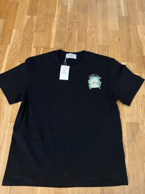 Svart t-shirt från Casablanca - Snygg svart t-shirt från Casablanca med ett färgglatt tryck och logga på bröstet. Klassisk rund hals och korta ärmar. Perfekt för dig som vill ha en stilren men ändå unik look.