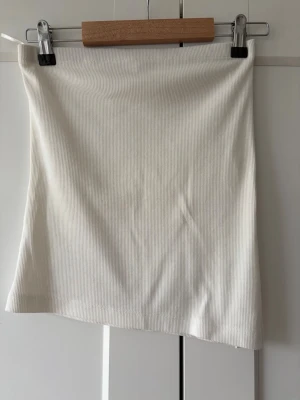 Vit ribbad topp med slits - Snygg vit ribbad topp med en liten slits på sidan. Toppen har en enkel och stilren design med rak passform och är gjord i ett stretchigt material som sitter bekvämt. Perfekt för varmare dagar och enkel att matcha med jeans eller en kjol.