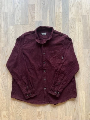 Eddie Bauer skjorta - vinröd, XL - Mycket bra skick. Inga tydliga tecken på användning Skjorta från Eddie Bauer, storlek XL, vinröd Knappstängning, bröstficka vänster med lapplogga, dubbelknapp ärmslut Bröstvidd: 59 cm Längd: 70 cm 100% bomull Inga defekter, normalt slitage