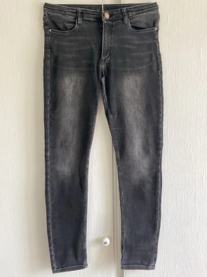 Svarta skinny jeans  - Säljer ett par svarta skinny jeans med lätt slitna detaljer och klassisk femficksmodell. Är du pysslig kan du göra en jeanskjol med verlang av dessa, (Tutorial på TikTok) Jeansen har en hög midja ocj materialet är stretchigt för extra komfort och de har en knapp och dragkedja framtill.💞