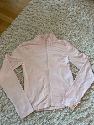 Ljusrosa jacka med dragkedja - Ljusrosa jacka med hel dragkedja framtill och hög krage. Tillverkad i ett mjukt och stretchigt material som ger en slim och sportig look. Jackan har långa ärmar och en enkel, stilren design utan synliga loggor.