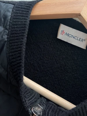 Svart Moncler cardigan - Säljer min Moncler-kofta i storlek XS.  Den är i ull och från en äldre modell (2017). Jag köpte den helt ny via reseller för ca 9 månader sedan. Jag använde den i ca 3–4 månader förra sommaren, och efter det har den mest legat i garderoben.  Skicket är mycket bra, nästan som ny utan tydliga defekter. Det finns tyvärr ingen originalförpackning eller kvitto.  Minsta pris jag kan sälja den för är 6 500 kr, eftersom denna ullmodell är ganska svår att hitta i den här material just nu