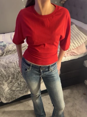 Röd croppad topp med knyt i ryggen - Från Gina tricot. Trendig röd topp med halvlånga ärmar och snygg knytning i ryggen. Toppen har en enkel, stilren design och är tillverkad i mjukt bomullsmaterial. Perfekt för dig som vill ha en cool och bekväm look.