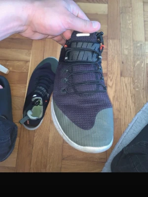 Svarta Nike sneakers med gröna detaljer - Säljer ett par svarta Nike sneakers med gröna detaljer och vit sula. Skorna har en stickad ovandel, svarta skosnören och orange detaljer vid snörningen. Swoosh-logga på sidan och dragflik bak för enkel påtagning.