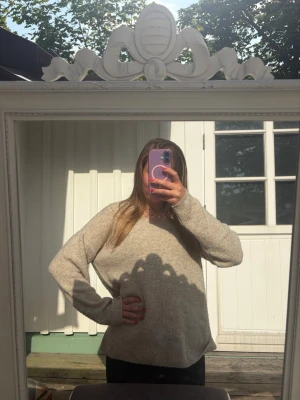 Beige stickad tröja med v-ringning - Mysig beige stickad tröja med v-ringad hals och avslappnad passform. Tröjan har långa ärmar och är tillverkad i ett mjukt, grovt stickat material som passar perfekt för kyligare dagar.