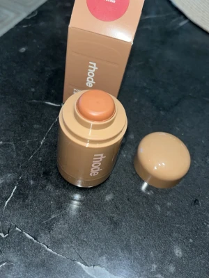 Rhode krämrouge i stickform - Krämrouge från Rhode i en smidig stickform. Färgen är en varm persikorosa nyans som ger kinderna en fräsch glow. Förpackningen är beige och kompakt, perfekt att ha med i väskan. Enkel att applicera direkt på huden för ett naturligt resultat.