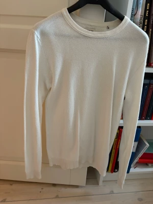 Vit Jack and Jones Tröja - Säljer en stilren vit stickad tröja med rund hals och lång ärm. Tröjan har ett diskret strukturmönster och ribbade muddar vid ärmslut och nederkant. Perfekt att matcha med jeans för en clean look