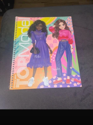 TOPModel ritbok - Säljer en färgglad TOPModel ritbok med spiralbindning. Omslaget har illustrationer av två modeller och insidan innehåller sidor med konturer av modeller att designa kläder på. Perfekt för dig som gillar mode och att rita egna outfits.