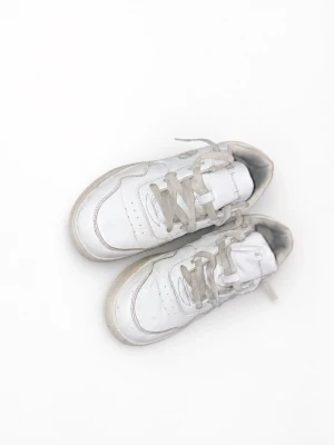 Vita låga sneakers med grå snören - Säljer ett par klassiska vita sneakers med lågt skaft och grå snören. Skorna har en stilren design med perforerade detaljer på sidan och är tillverkade i syntetmaterial. Perfekta för en clean och enkel look.