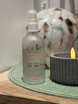 Loelle Rose Water Face Mist - Använd enligt bilderna. Fräsch ansiktsmist från Loelle med ekologiskt rosenvatten. Kommer i en frostad plastflaska med spraymunstycke och guldiga detaljer. Passar perfekt för att återfukta och ge glow till huden. Doftar naturligt av rosor och är pH-balanserande.