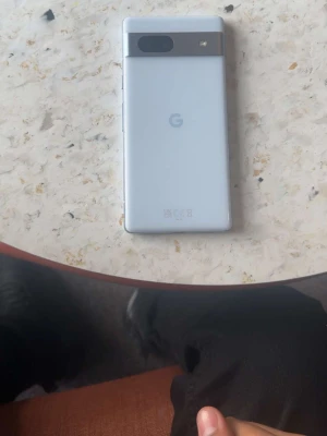 Blå Google Pixel mobiltelefon 7a - Säljer en vit Google Pixel med stilren design och en tydlig kameramodul på baksidan. Telefonen har en matt finish och den klassiska G-loggan. Kameran och blixten sitter i ett horisontellt fält högst upp. Perfekt för dig som gillar enkel och modern stil.KRYPTERAD MOBIL GRAPHENE OS