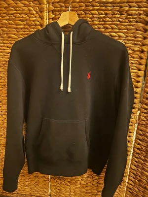 Svart hoodie med röd logga - En fett Ralph lauren hoodie, lite små defekter på snörena eftersom min hund har bitti på dem. Riktigt skön hoodie.  Skick 7/10