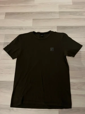 Boss T-shirt  - En stilren svart t-shirt i storlek L med rund hals och korta ärmar. På bröstet sitter en liten fyrkantig patch med logga. Perfekt basplagg till garderoben och enkel att matcha med allt.
