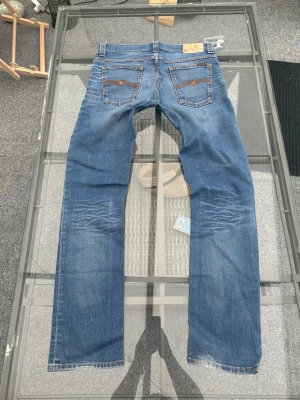 Nudie Jeans Grim Tim – Dark Used Denim (W33/L34) - Säljer ett par riktigt snygga Nudie Jeans i den populära modellen "Grim Tim". Tvätten heter "Dark Used Denim" och ger byxorna en perfekt, insliten look med snygga skuggningar och detaljer. Modellen har en smal passform med normalhög midja, och tack vare 2% elastan i tyget är de både följsamma och superbekväma att ha på sig hela dagen.  Modell: Grim Tim.  Tvätt: Dark Used Denim.  Storlek: W33 L34.  Material: 98% bomull, 2% elastan (skön stretch).  Skick: Fint begagnat skick med klassisk Nudie