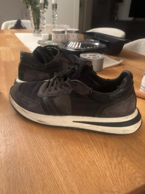 Svarta sneakers från Philippe Model - Säljer ett par svarta sneakers från Philippe Model med grå detaljer och vit sula. Skorna har en klassisk låg design, snörning och kombinerar mocka och textilmaterial för en cool look. Perfekta för dig som vill ha stil och komfort.