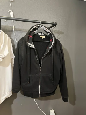 Burberry zip up - Säljer nu min Burberry zip up då den inte används längre och bara ligger i garderoben.  Bild 3 så ser man att den gått sönder lite men det är inget som syns när den är på. Storlek L men jag som har M så sitter den väldigt bra. Det är bara o ställa frågor osv