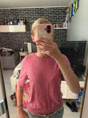 Rosa kortärmad topp - Söt rosa topp med rund halsringning och korta ärmar. Toppen har en enkel, klassisk design och är gjord i ett mjukt material som känns skönt mot huden. Perfekt att matcha med jeans eller kjol för en avslappnad look.